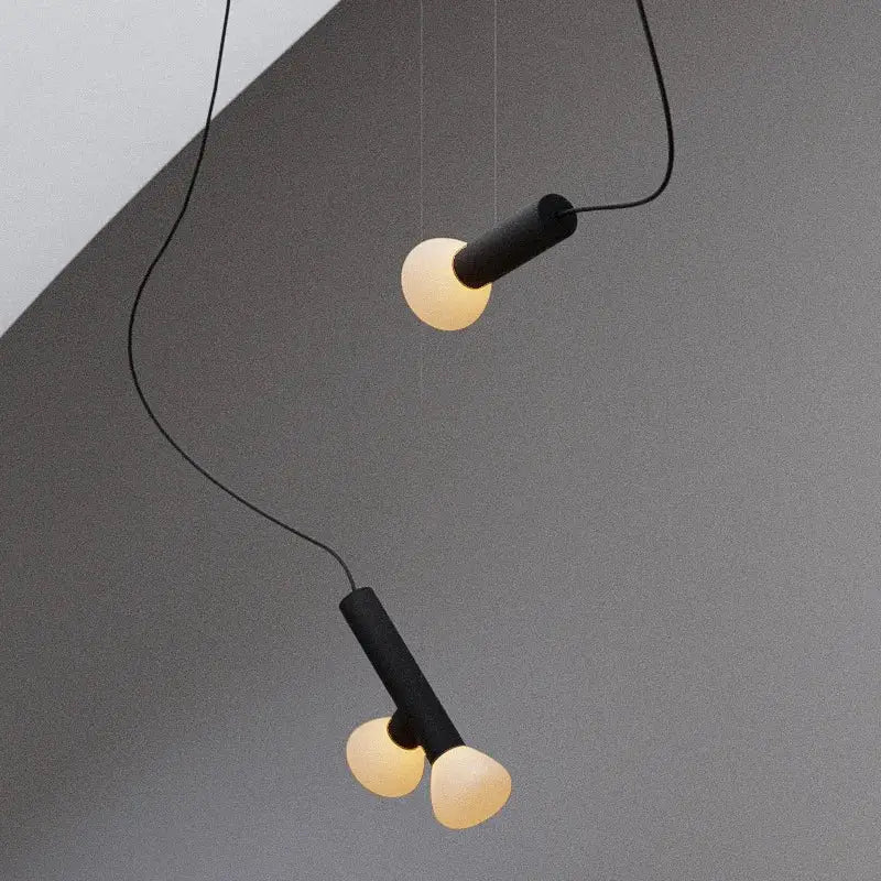 Minimalist black and white glass pendant lights with frosted globes hang from cords against a gray wall for dining room
