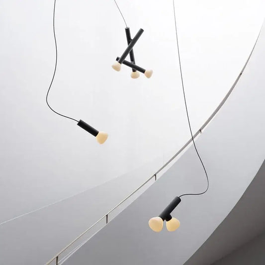 Minimalist black and white glass pendant lights with cylindrical black shades and off-white bulbs for dining room use
