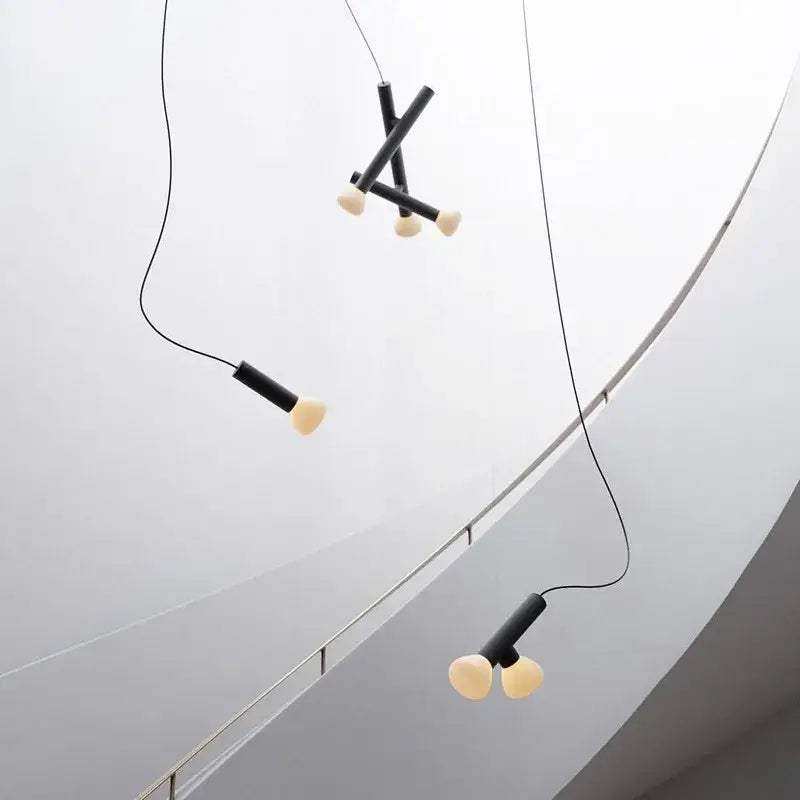 Minimalist black and white glass pendant lights with cylindrical black shades and off-white bulbs for dining room use