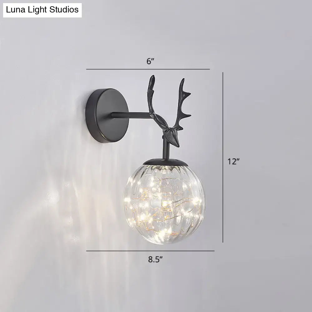Black metal deer antler wall sconce with clear textured glass globe and warm fairy lights for bedroom use