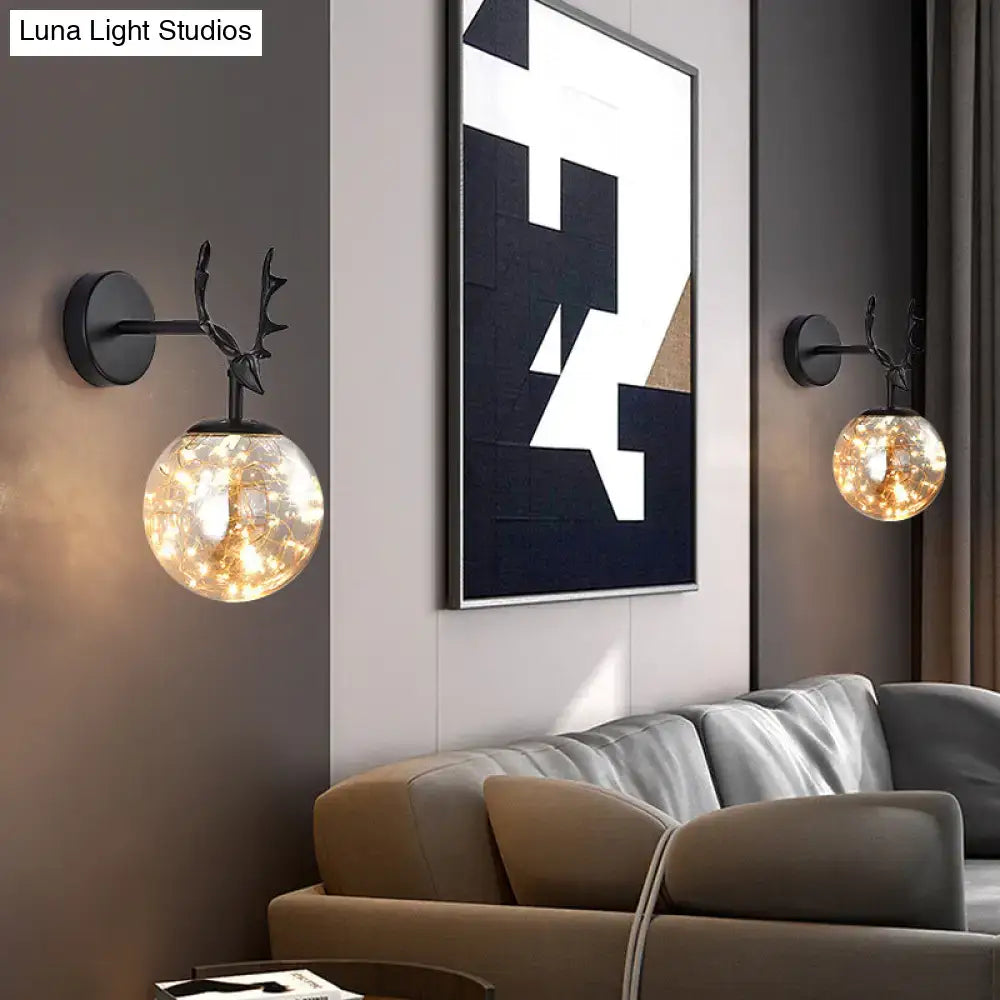 Black deer-head wall sconce with minimalist black antler design and spherical glass globe housing warm fairy lights