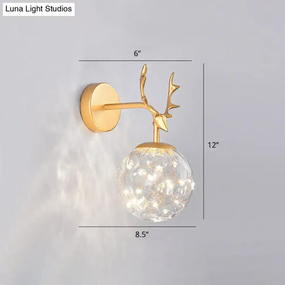 Minimalist gold-toned deer antler wall sconce with clear glass globe and warm white LED lights for bedroom fairy lighting