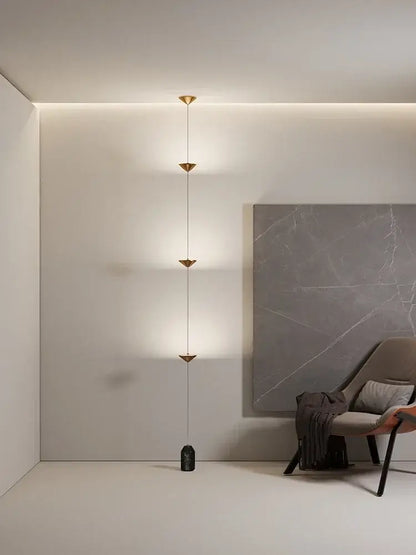 Minimalist black decorbites cone design floor lamp with gold-toned chain and four triangular lights on dark stone base