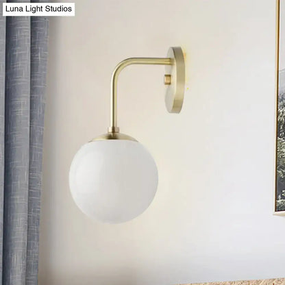 A minimalist golden black wall light with a sleek brass finish and a milky glass ball shade for bedroom use