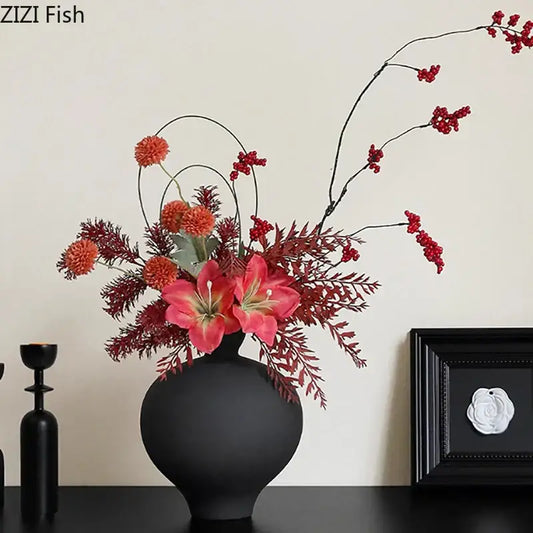 Minimalist black matte big belly ceramic vase holding vibrant artificial red and pink flowers with berry accents
