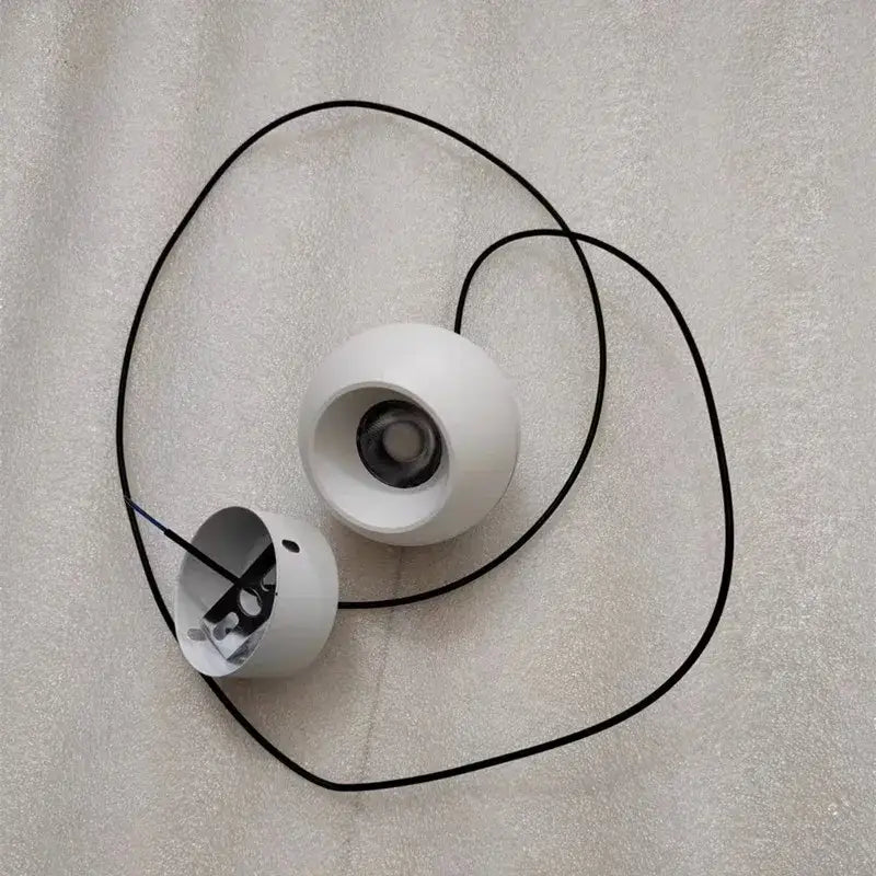 White spherical wireless speakers with black audio cables beside minimalist black and off-white die-cast aluminum pendant light with acrylic lamp holder for kitchen