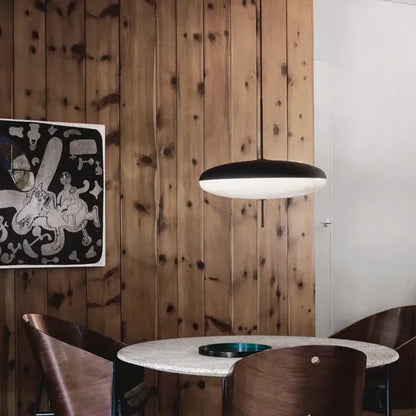 Minimalist black and white acrylic pendant light with a sleek modern disc design hanging above a dining table