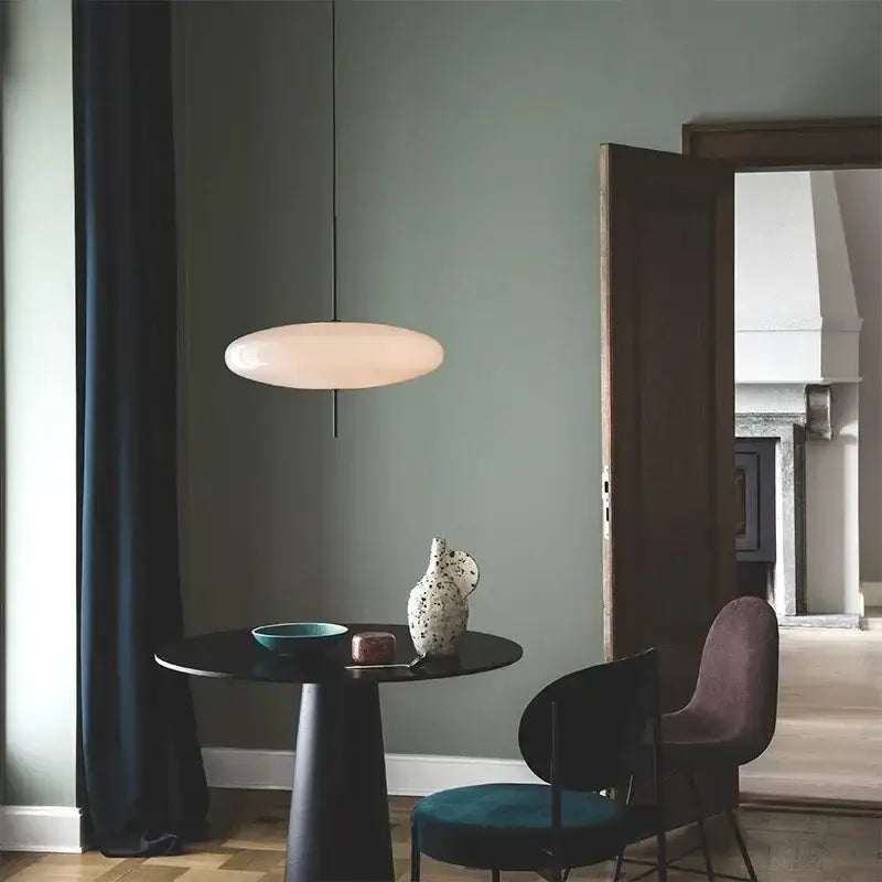 Minimalist black and white acrylic pendant light with a matte off-white disc shade suspended by a thin black cord for dining room