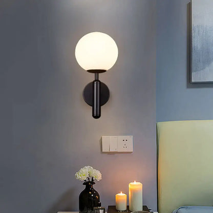 Modern black wall mount light with frosted glass globe shade and minimalist brass textured finish for bedroom use
