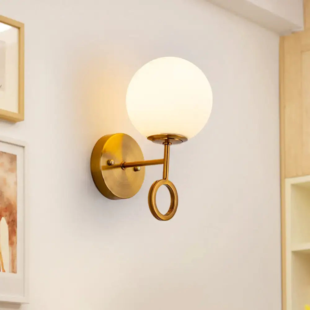 Minimalist brass wall sconce with cream glass shade frosted globe and ornamental ring accent for bedroom lighting