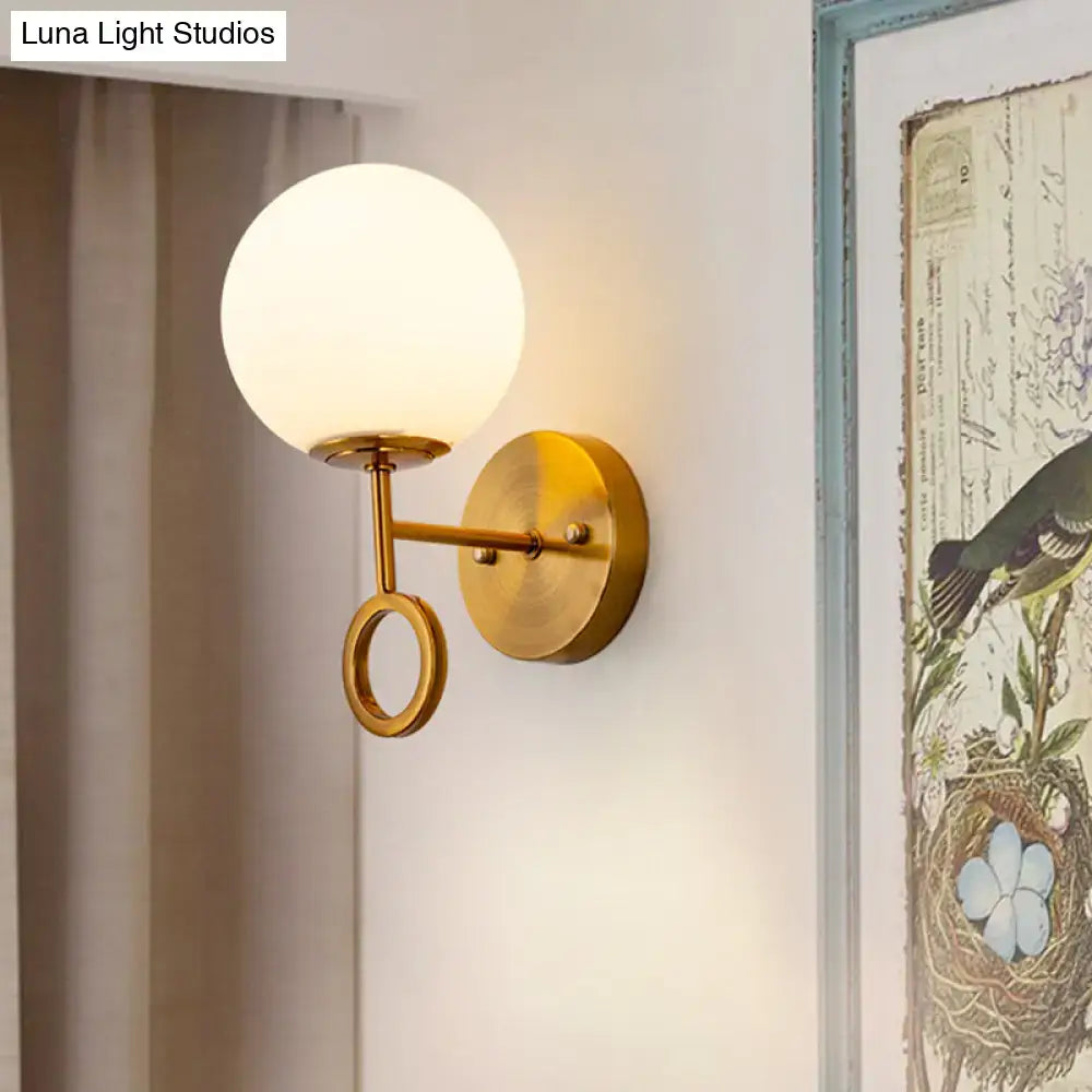 Minimalist brass wall sconce with gold tone finish and cream glass shade featuring a frosted globe and circular ring
