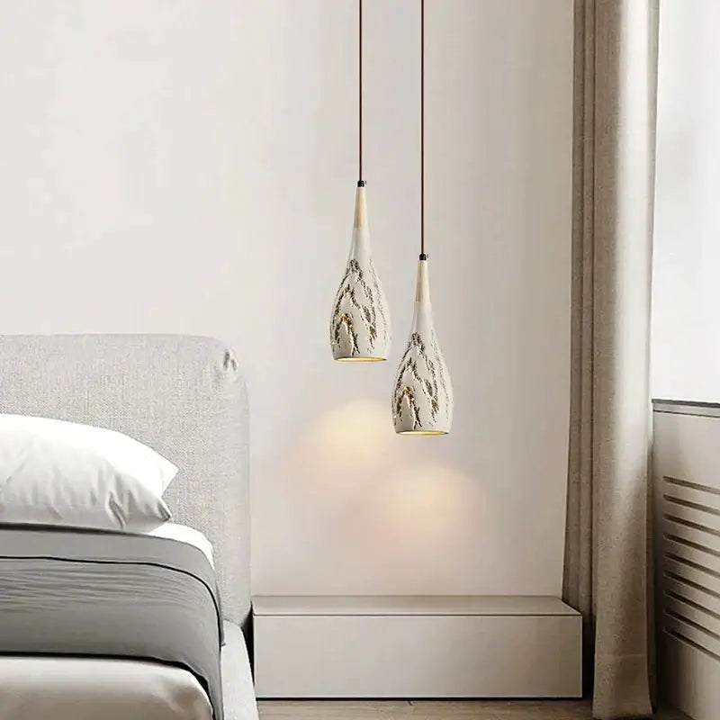 Two elegant white ceramic pendant chandelier lights with gray leaf patterns hang from cords on decorbites concrete ceiling