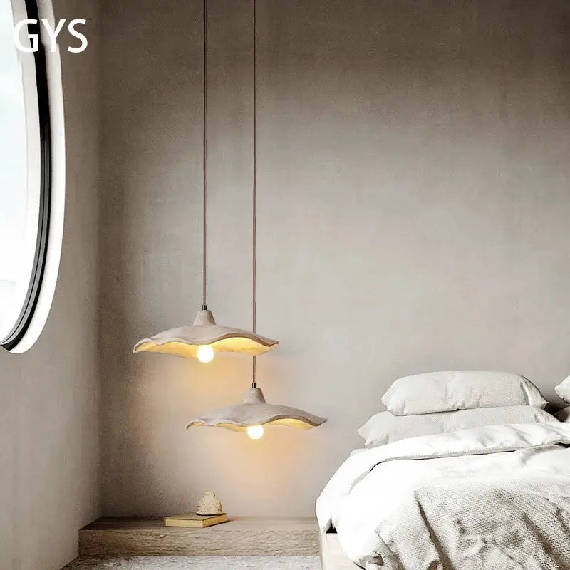 Two minimalist ceramic petal pendant chandelier lights with soft white shades hanging from cords on a concrete ceiling