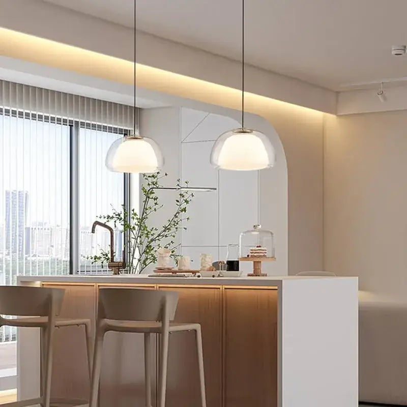 Two modern minimalist clear glass jelly pendant lamps with frosted domes hang above a kitchen island