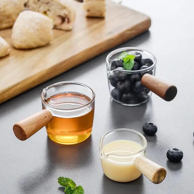 Minimalist clear glass sauce dish with wooden handle featuring three glass sauce dishes filled with liquids and mint leaves