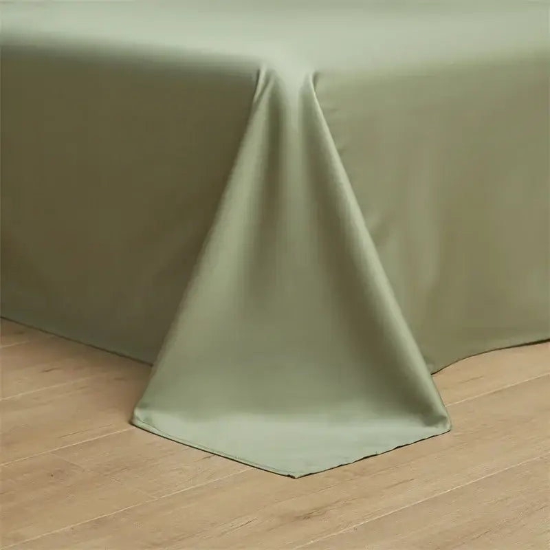 A smooth sage green egyptian cotton solid tablecloth drapes over wood in a minimalist cream and green bedding set bedroom
