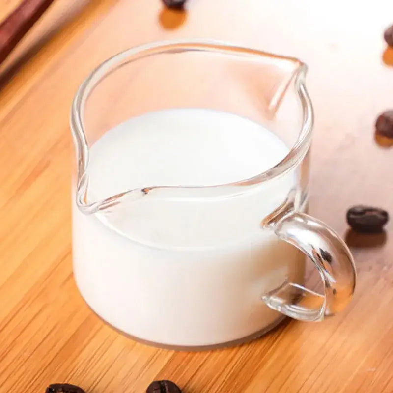 Clear glass pitcher filled with white milk on wooden surface from minimalist double mouth glass milk cup set