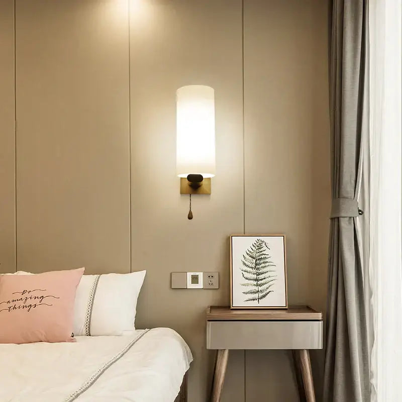 A minimalist wooden wall lamp with a frosted glass shade and brass base for bedroom use with pull chain