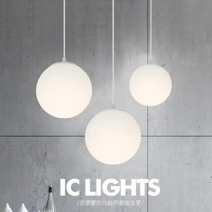 Three minimalist frosted white acrylic globe pendant lights with brushed nickel cords hang against a concrete wall
