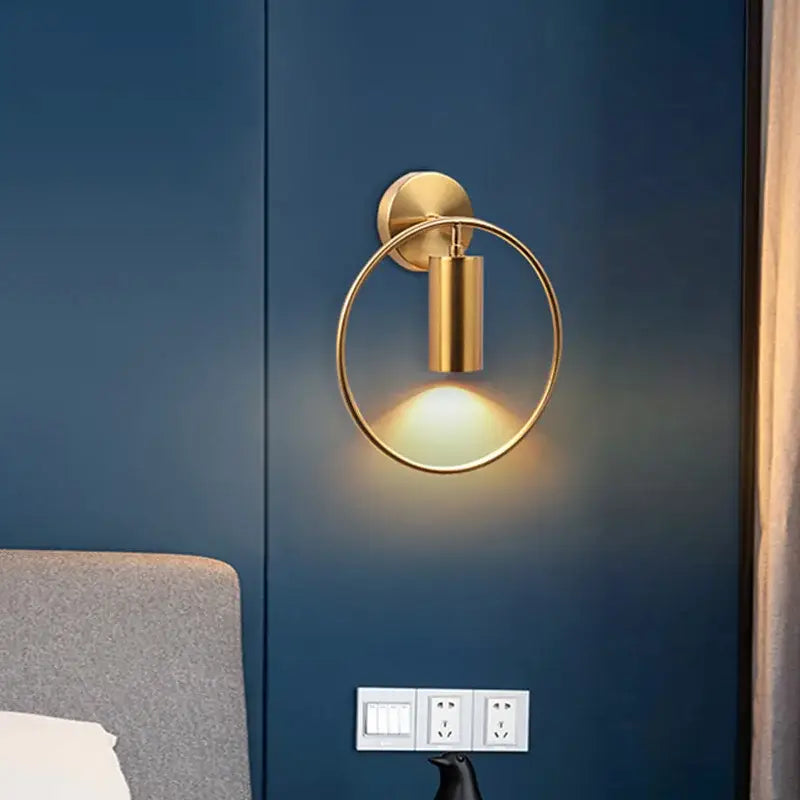 Minimalist gold-toned decorbites wall light with circular ring and adjustable angle cylindrical fixture for bedroom decor