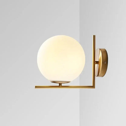 Minimalist gold wall sconce with frosted white glass ball emitting warm white light for bedroom lighting