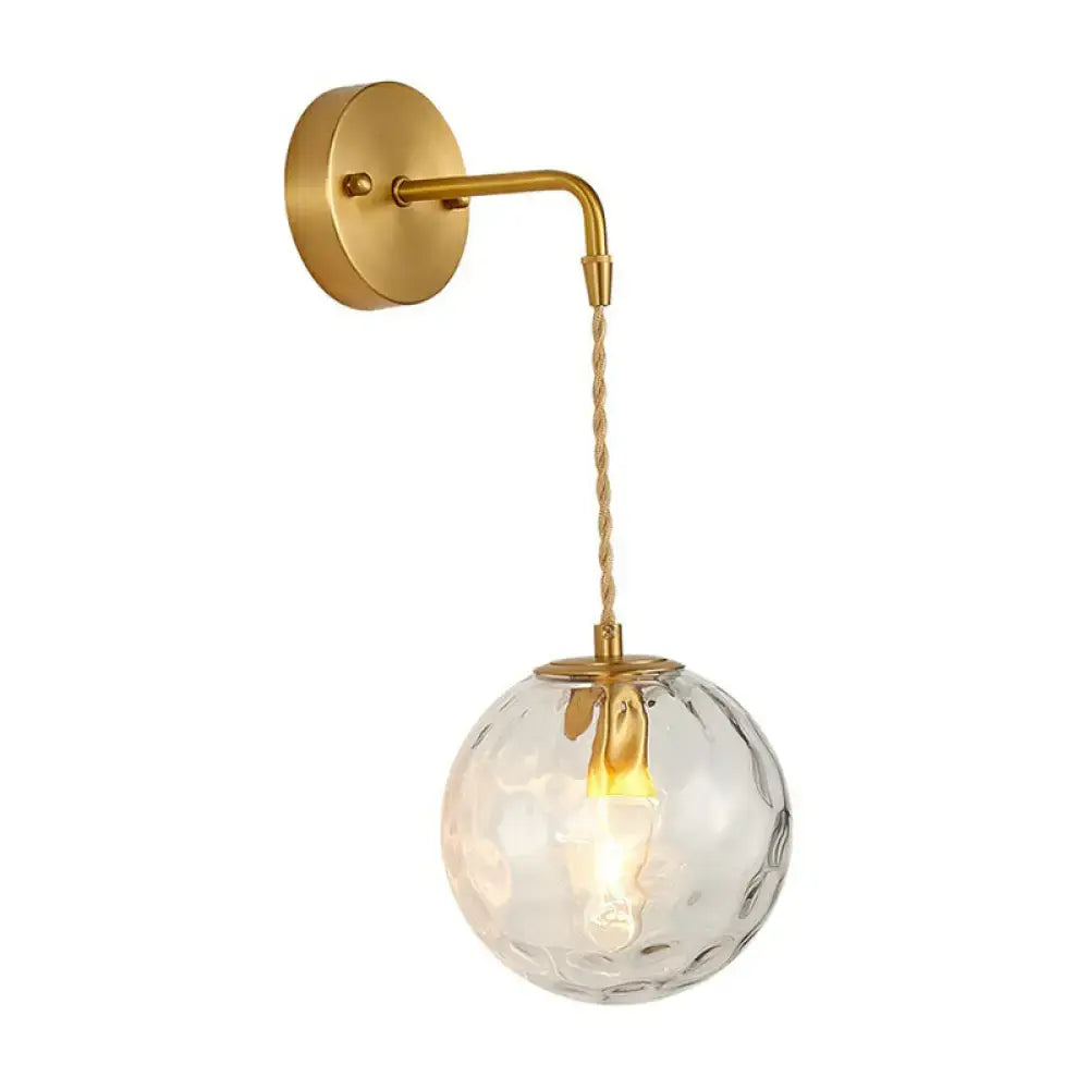 Gold ball sconce with hammered glass shade featuring a textured clear globe and twisted cord for bedroom lighting