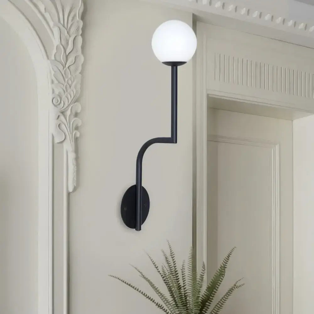 Black metal wall sconce with long curved arm and opal glass spherical frosted globe for minimalist bedroom decor