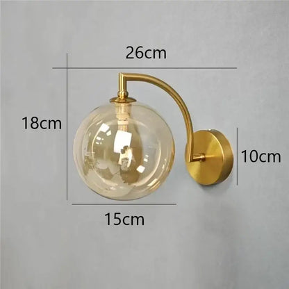 Minimalist gold wall sconce with clear glass ball and curved arm designed as a bedroom wall lamp