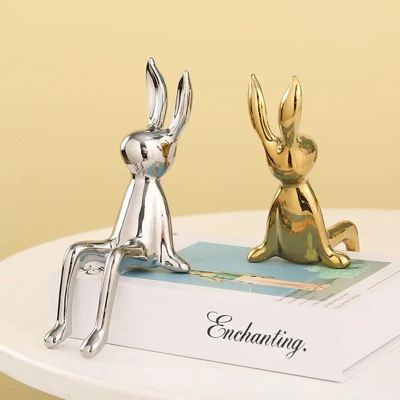 Two sleek gold and silver rabbit ceramic ornaments sitting upright on a book for decorbites gold rabbit decor