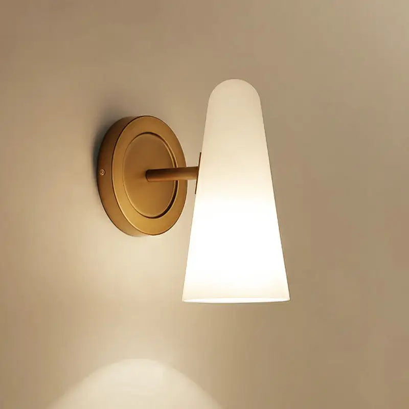 A minimalist gold wall sconce light with a sleek brass body and frosted glass shade for living room use