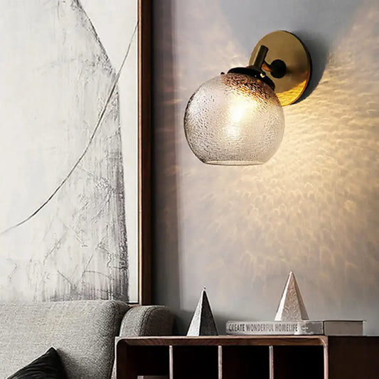 Minimalist gold-toned wall sconce with textured frosted glass globe for living room lighting and decor