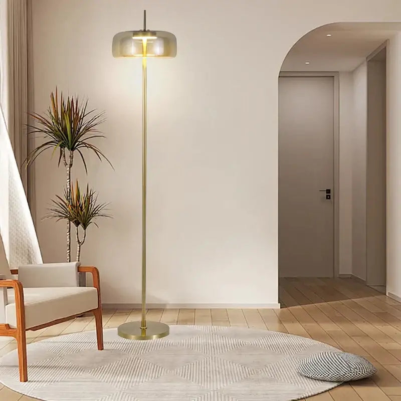 Minimalist floor lamp with gray glass floor shade and brass finish emitting warm light for living room use
