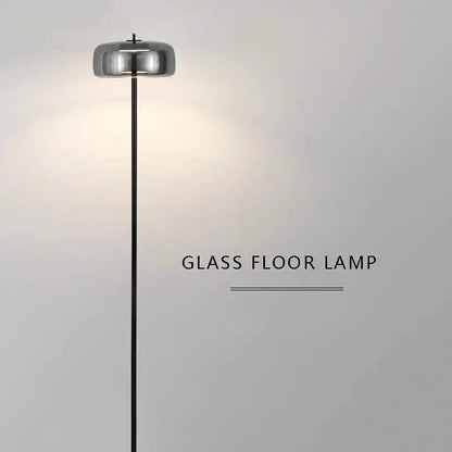 Minimalist gray glass floor lamp with a sleek chrome cylindrical shade and black metal stand for living room use
