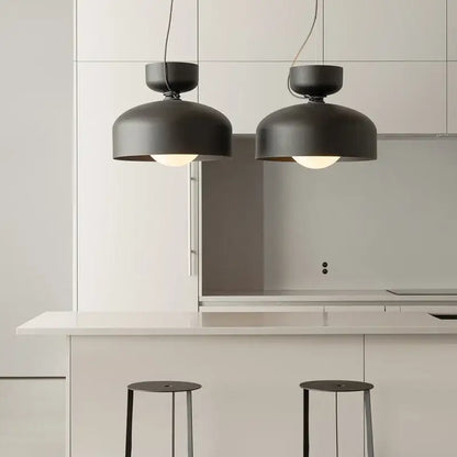 Two matte black minimalist pendant lights with decorbites forged iron hang above a white kitchen island
