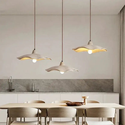 Three off-white ceramic pendant chandeliers with scalloped edges hang above a dining table in minimalist decorbites concrete high style