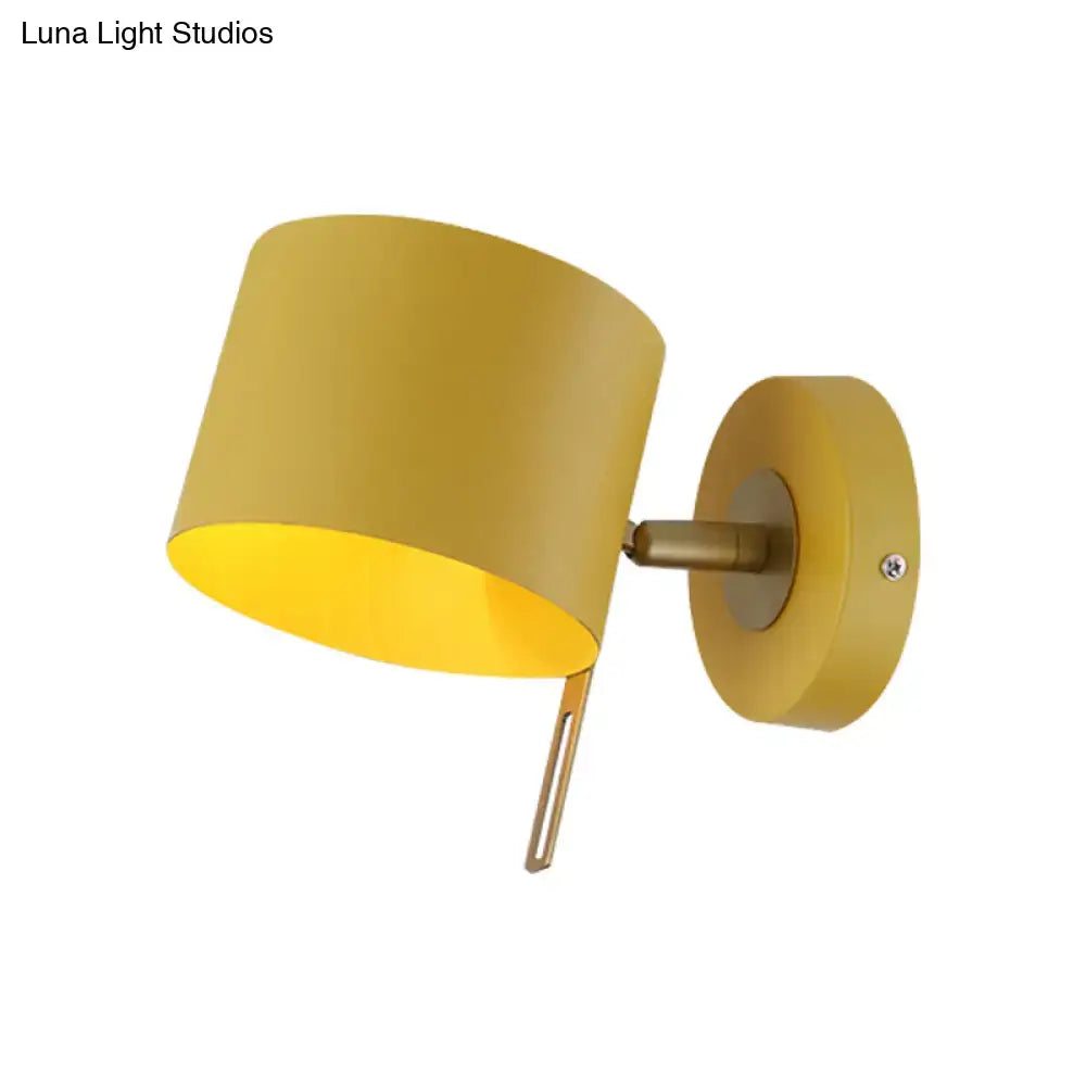 Minimalist yellow cylindrical wall sconce with matte finish and brass accents for corridor lighting with pink hues