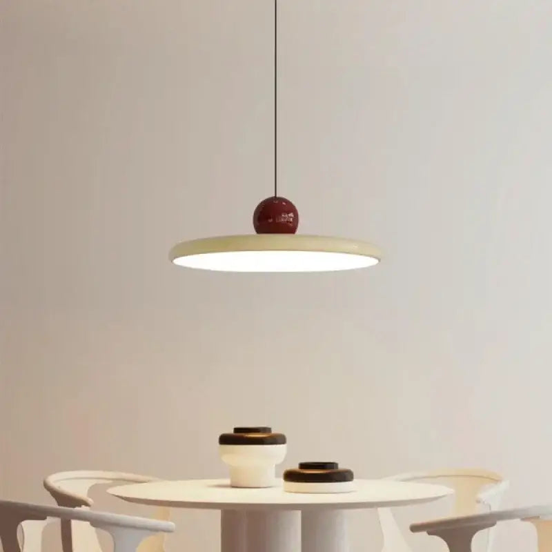 Minimalist red and white acrylic pendant light with glossy spherical top and flat shade suspended by thin cord pendant