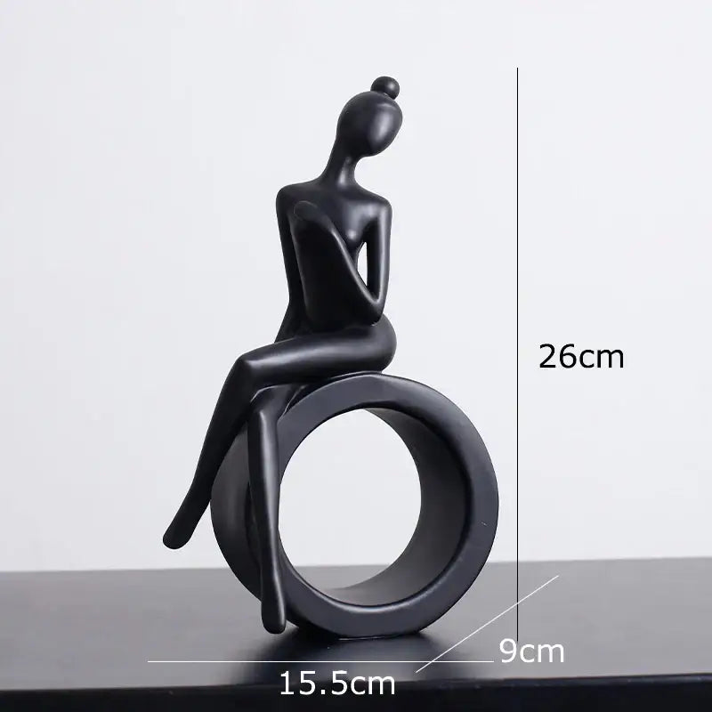 Black matte-finished abstract figures sculpture of a seated woman with hair in a bun on a circular ring base for decor