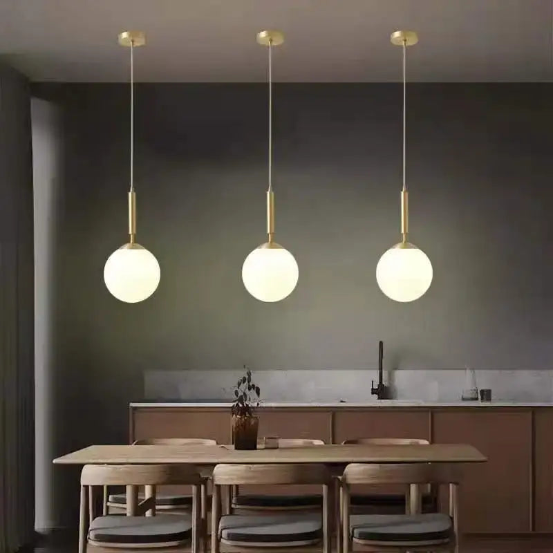 Minimalist white glass ball pendant light with frosted glass shades and gold fixtures in a modern dining room decorbites glass ball