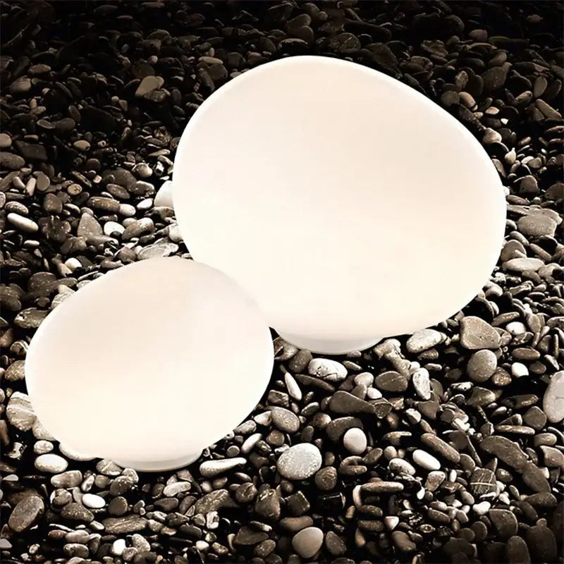 Two smooth white oval-shaped bowls on dark pebbles in minimalist white decorbites goose egg led floor lamp setting