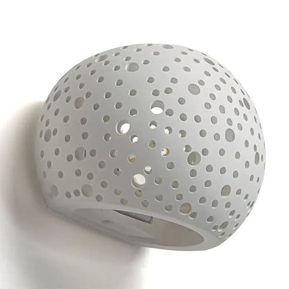 Minimalist white spherical gypsum wall lamp with circular perforations providing diffused light for living room