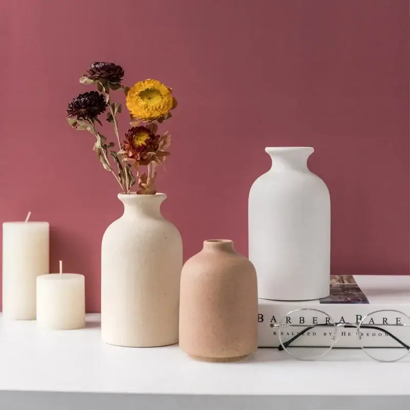 Cream-colored decorbites ceramic vase with rounded body and narrow neck holding dried flowers for dining room decor
