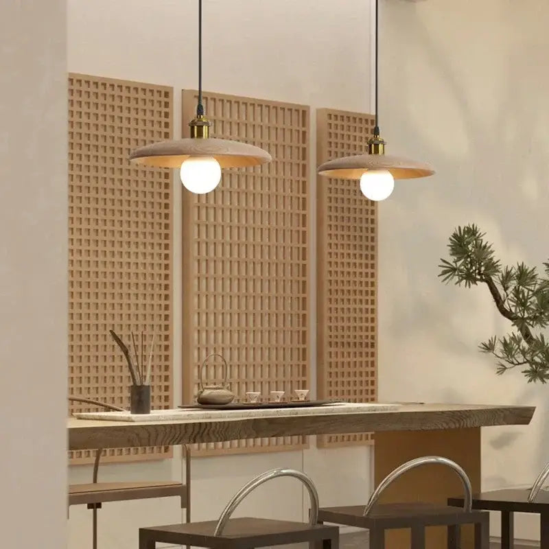 Two minimalist pendant lights with matte beige shades and brass hardware feature led bulb with three-color dimming above wood table