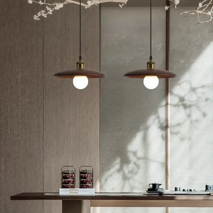 Two warm-toned minimalist wood and brass pendant lights with led bulb hang above a wooden dining table