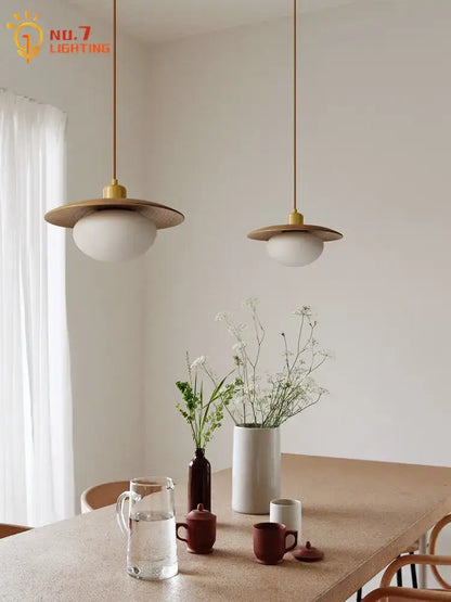 Two minimalist wood and brass pendant lights with cream wind frosted glass globes hanging above dining table