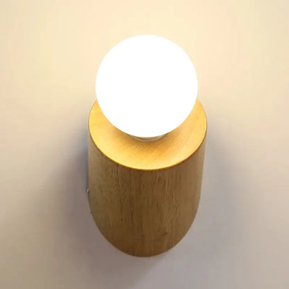 Minimalist wall lamp with warm wood cylindrical base and frosted white light bulb for bedroom or living room use