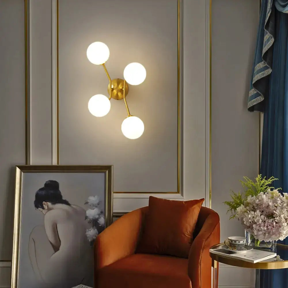 Gold-toned brass branch wall light with four spherical frosted glass globes ideal as a bedroom wall lamp