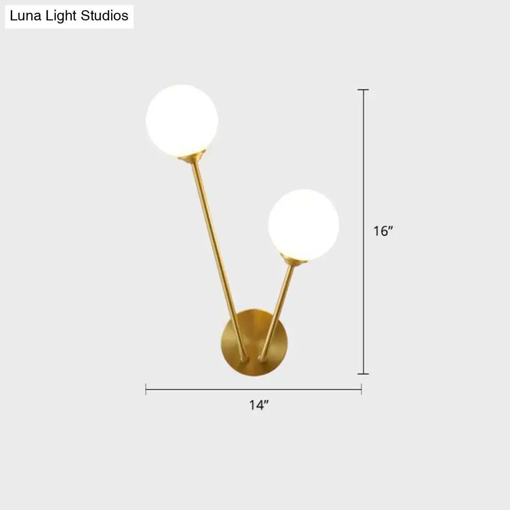 Minimalistic brass branch wall light with gold-toned finish and two spherical frosted glass shades for bedroom use