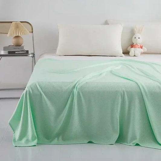 A mint green bamboo fiber cooling summer blanket with a subtle woven diamond quilt pattern draped over a mattress