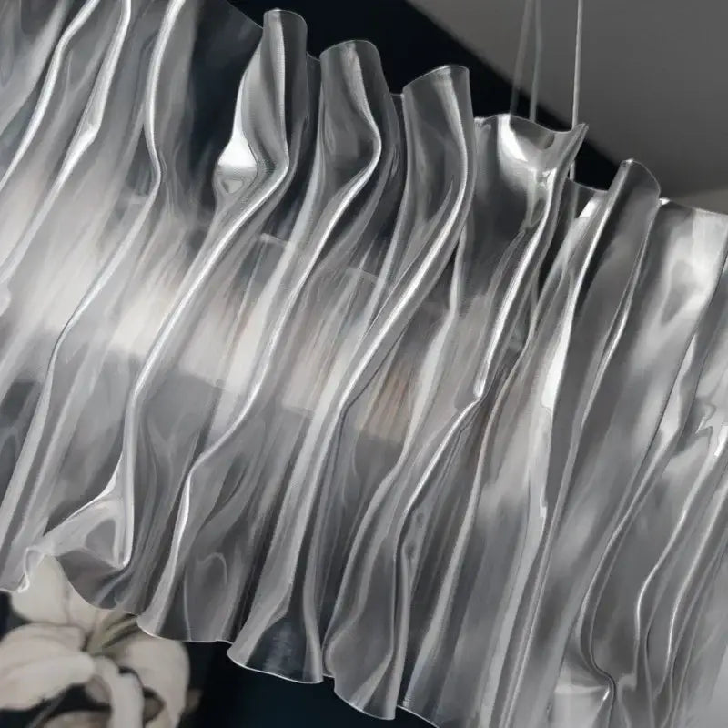A modern acrylic ceiling chandelier with flowing wave-like ridges and a gold ring light for dining room use